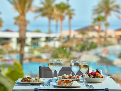 Mesa puesta con vino y aperitivos frente a una piscina y palmeras de fondo.