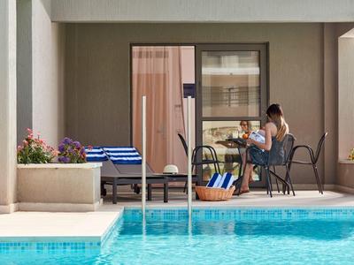 Ein blauer Pool vor einer Terrasse, auf der zwei Personen am Tisch sitzen und reden.