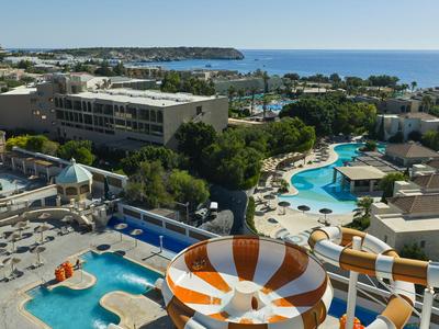 Vista de un resort con piscinas, toboganes acuáticos y tumbonas junto al mar.