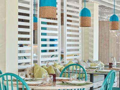 Moderne Café-Innenansicht mit türkisfarbenen Stühlen, runden Tischen und hängenden Lampen.