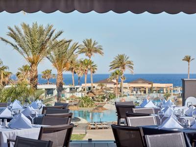 Blick von einem Restaurant auf einen Pool mit Palmen und Blick aufs Meer.