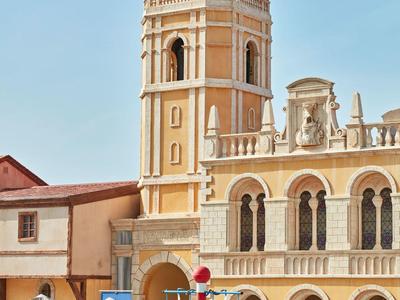 Gelbes historisches Gebäude mit hoher Turmspitze und Arkaden unter klarem Himmel.