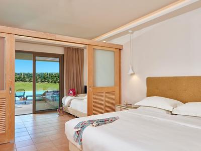 Modernes Hotelzimmer mit großem Bett, Schiebetüren und Blick auf Terrasse mit grünem Garten.