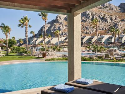 Moderner Pool mit Liegestühlen, Palmen und Bergen im Hintergrund bei sonnigem Wetter.