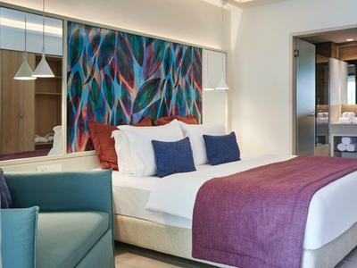 Modernes Hotelzimmer mit großem Bett, buntem Kopfteilstoff und Sitzgelegenheit.