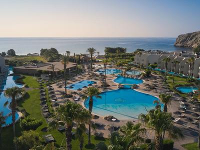 Vista de un resort con piscinas, palmeras y el mar de fondo al atardecer.