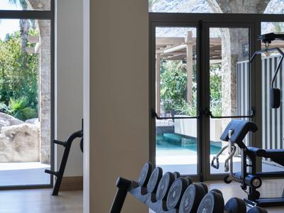 Gimnasio moderno con mancuernas y máquinas, vista a piscina exterior a través de grandes ventanas.