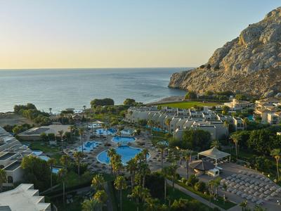 Vista de un hotel con piscina y jardín en la costa al atardecer.