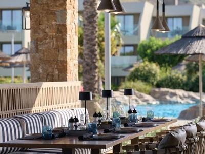 Zewnętrzny obszar restauracyjny hotelu z pasiastymi poduszkami i widokiem na basen.