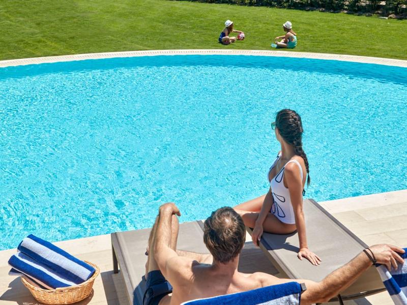 Zwei Personen entspannen sich an einem runden Pool auf blauen Liegestühlen im Freien.