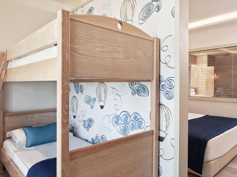 Kinderzimmer mit Holz-Etagenbett, blauer Bettwäsche und Tapete mit Blumenmuster, angrenzendes Schlafzimmer.