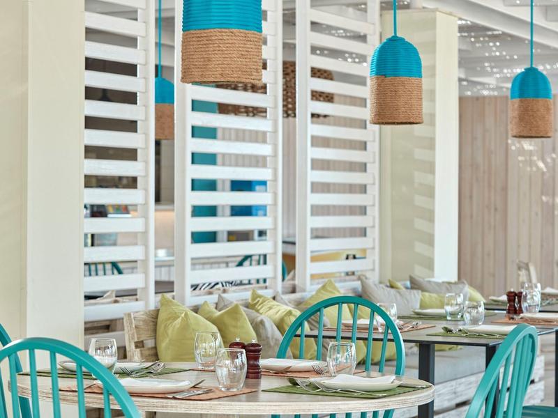 Moderne Café-Innenansicht mit türkisfarbenen Stühlen, runden Tischen und hängenden Lampen.