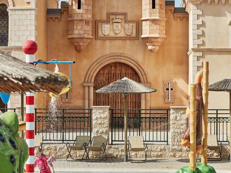 Freizeitpark mit Wasserbecken, bunten Skulpturen und einem historischen Gebäude im Hintergrund.