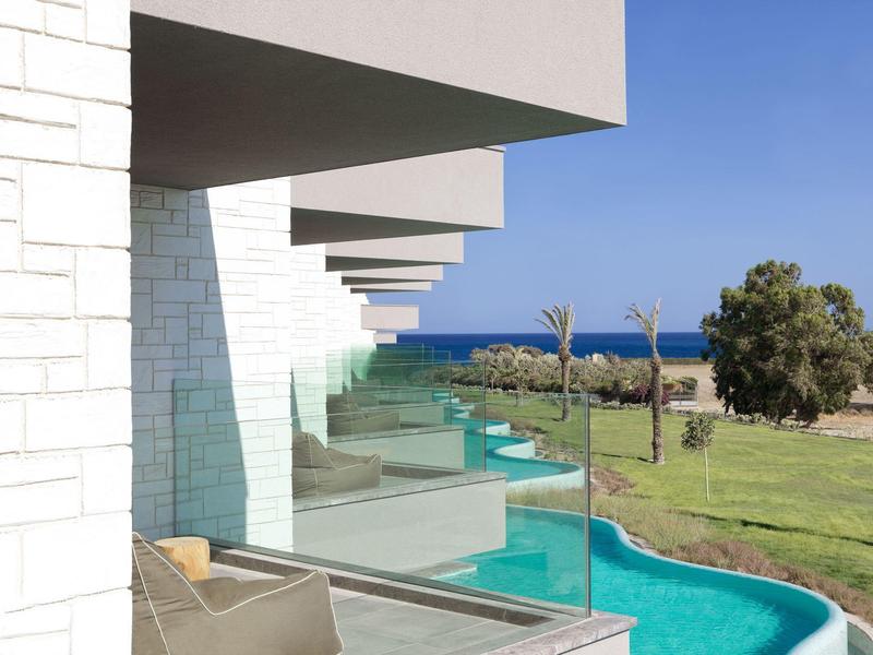 Moderne Gebäude mit Glasbalustraden, Blick auf grünen Rasen und blaues Meer im Hintergrund.