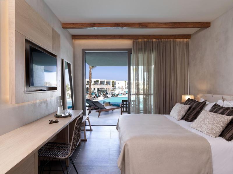 Modernes Hotelzimmer mit Doppelbett, Flachbildschirm, Schreibtisch und Blick auf Poolterrasse.