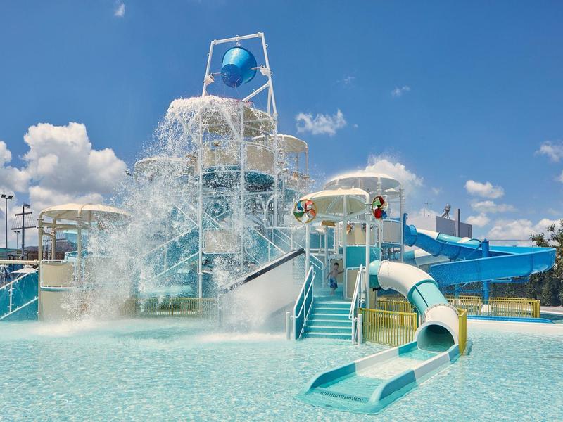 Wasserpark mit Rutschen, großen Wassereimern und klarem blauem Himmel im Hintergrund.
