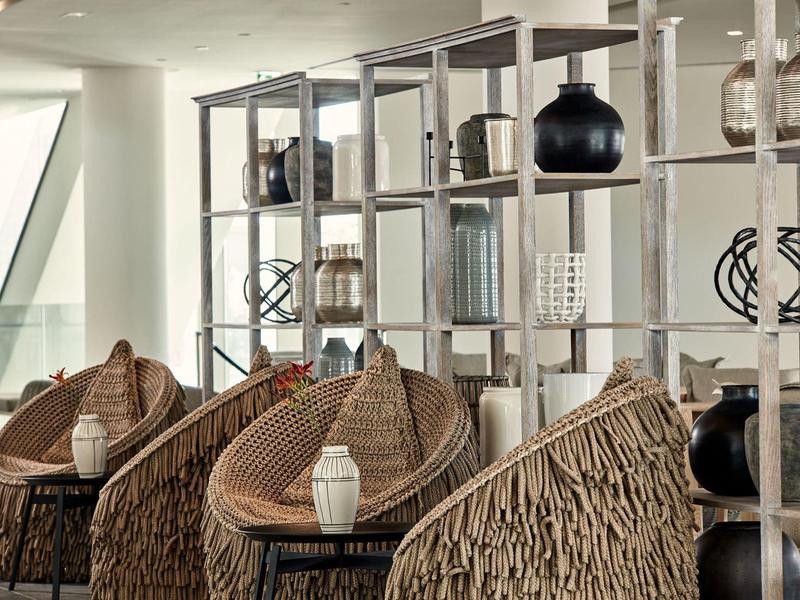 Heller Raum mit drei geflochtenen Sesseln und offenen Regalen mit Vasen und Dekorationen.
