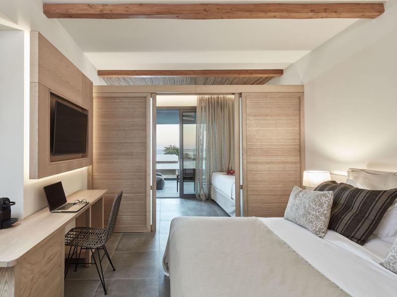 Modernes Schlafzimmer mit Holzdecke, großem Bett, Schreibtisch und Zugang zu Balkon mit Meerblick.