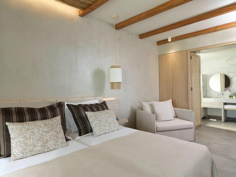 Modernes Schlafzimmer mit Doppelbett, hellen Wänden, Holzdeckenbalken und gemütlichem Sessel.