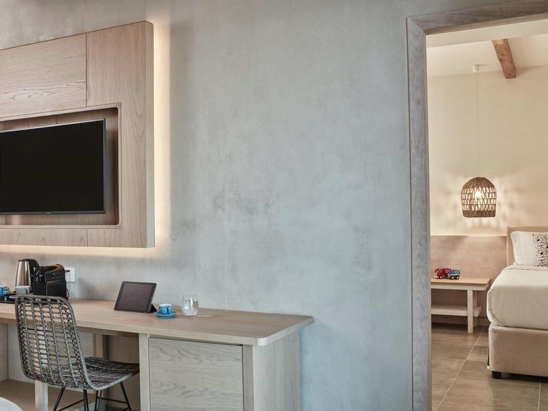 Moderner Arbeitsplatz mit Holztisch, Laptop, Stuhl aus Metall und angrenzendem Schlafzimmer mit Doppelbett.