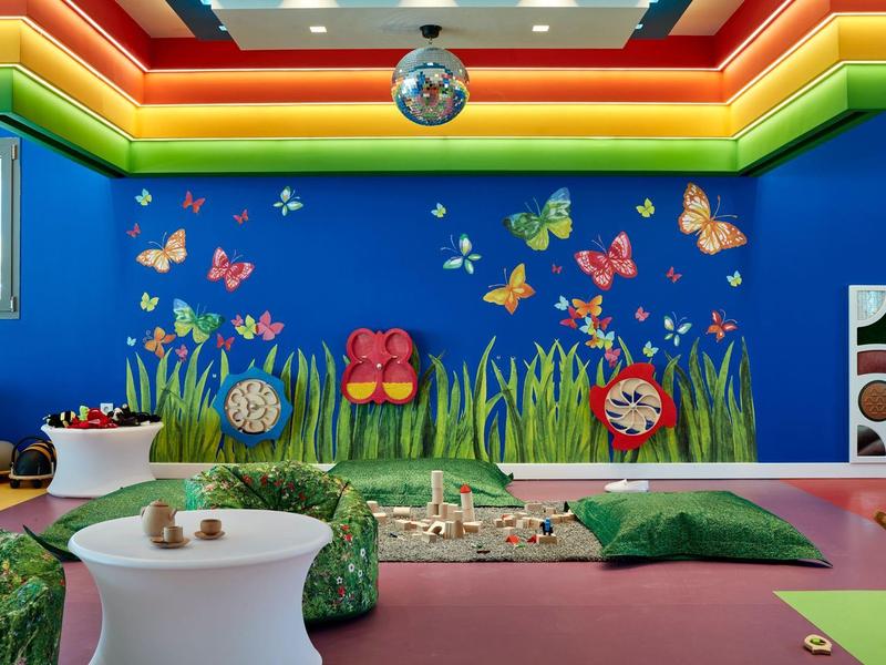 Bunten Kinderspielraum mit blauer Wand, Schmetterlingen, grünen Kissen und verspielten Möbeln.