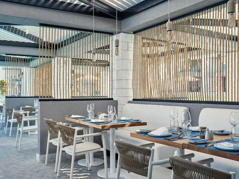 Modernes Restaurant mit Holztischen, Stühlen und großen Fenstern, hell und luftig gestaltet.