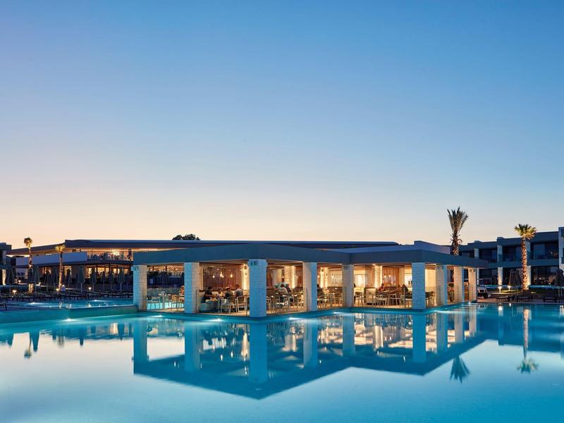 Großer, beleuchteter Pool mit Pavillon und Spiegelung, vor klarem Abendhimmel.