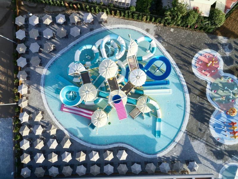 Vogelperspektive auf ein farbenfrohes Wasserparkbecken mit Wasserrutschen und Schatten spendenden Sonnenschirmen.