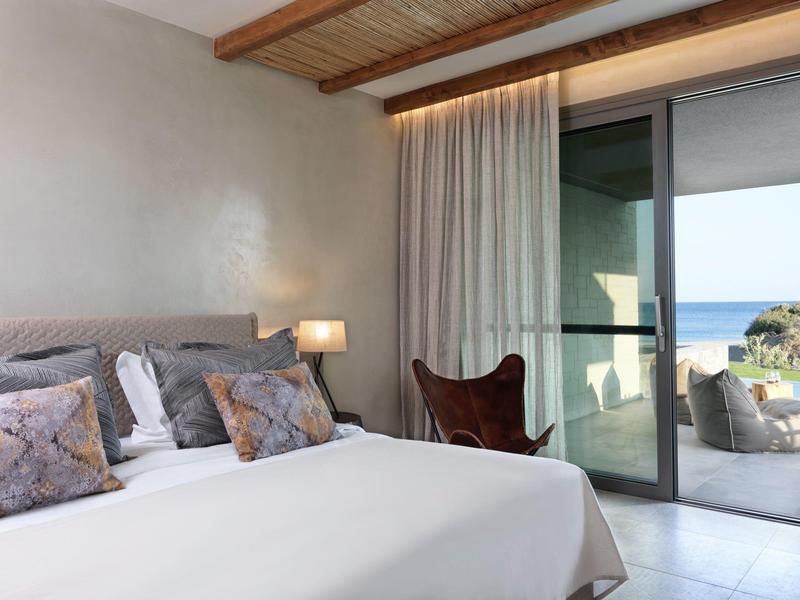Schlafzimmer mit großem Bett, weißen und grauen Kissen, Holzdecke, Lampe und Balkon mit Meeresblick.
