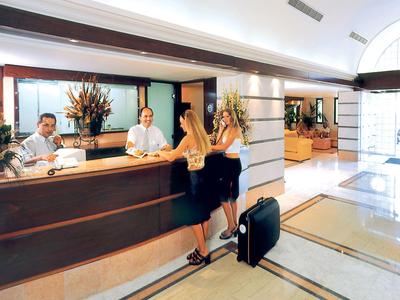 Hotelrezeption mit zwei Gästen, zwei Angestellten, hellem Fußboden und modernem Empfangstresen.