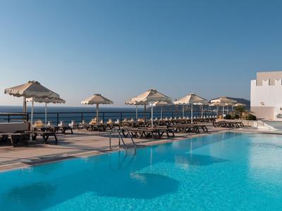 Poolbereich mit Sonnenliegen und Schirmen neben dem Meer unter klarem Himmel