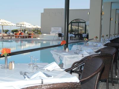 Außenrestaurant mit weißen Tischen und Blick auf den Pool und das Meer.
