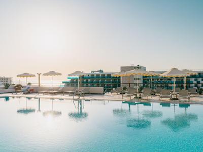 Großer Hotelpool mit Sonnenliegen und Sonnenschirmen bei Sonnenuntergang.