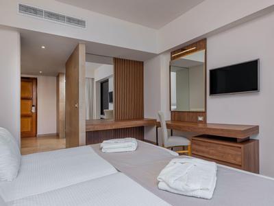 Modernes Hotelzimmer mit weißer Bettwäsche, Handtüchern und Flachbildfernseher an der Wand.