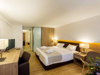 Helles Hotelzimmer mit Doppelbett, zwei Nachttischen, Schreibtisch und Stuhl, moderne Einrichtung.