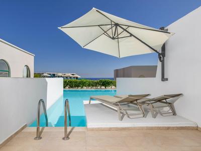 Poolterrasse mit zwei Liegestühlen, Sonnenschirm und Blick auf das Meer bei klarem Himmel.