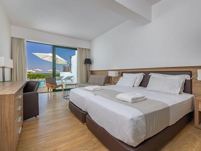 Helles Hotelzimmer mit zwei Einzelbetten, Holzboden und Balkon mit Meerblick.