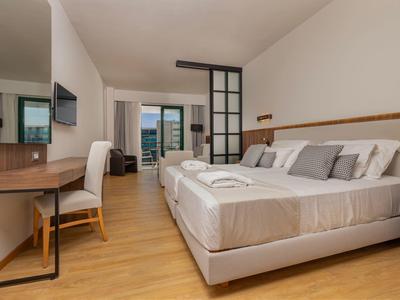 Modernes Hotelzimmer mit zwei Betten, Schreibtisch, TV und Balkon mit Meerblick.