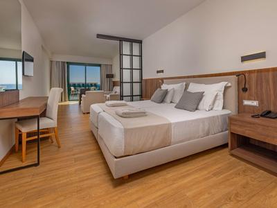 Modernes Hotelzimmer mit Doppelbett, Schreibtisch, Stuhl und Blick auf die Stadt durch das Fenster.