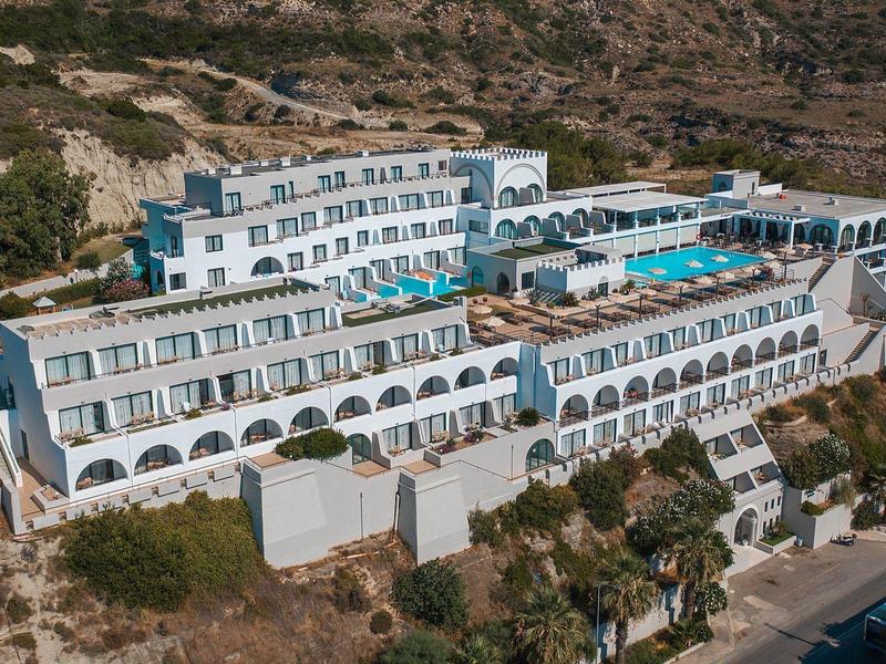 Großes, weißes Hotelgebäude mit mehreren Etagen, blauen Fensterläden und einem Pool, umgeben von Bergen.