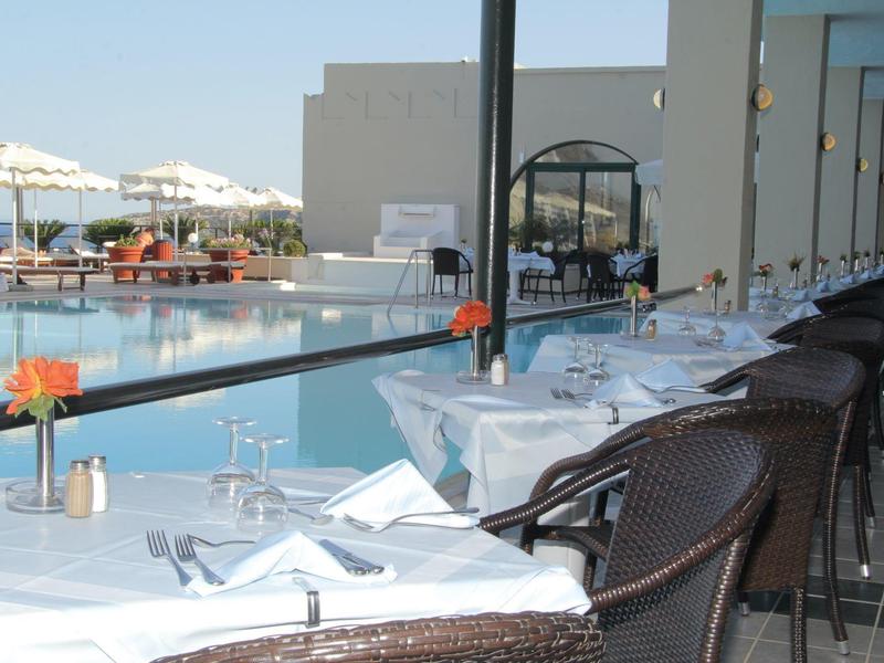 Terrassenrestaurant mit gedeckten Tischen, dunklen Stühlen und Blick auf Pool und Meer bei Sonnenschein.
