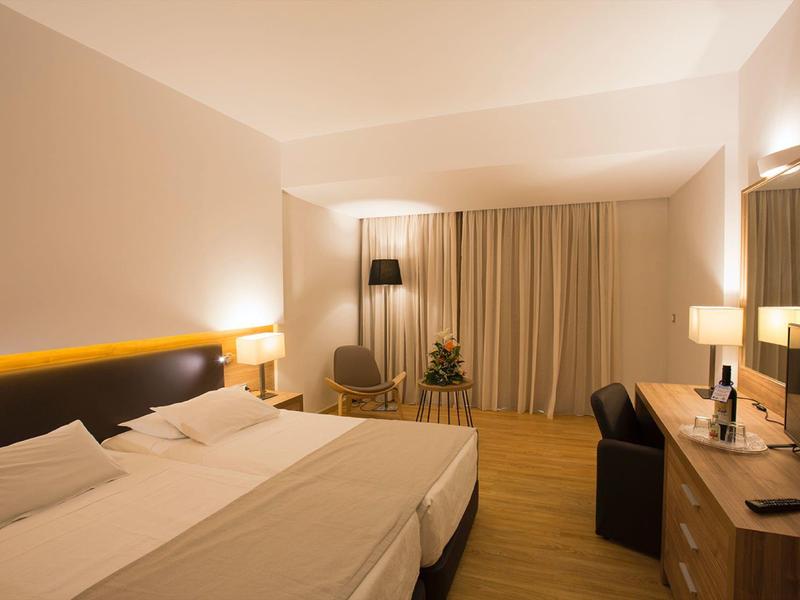 Modernes Hotelzimmer mit zwei Einzelbetten, Schreibtisch, Stuhl und Vorhängen.