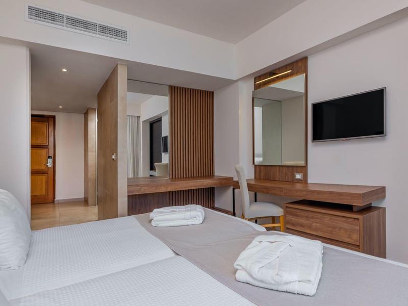 Modernes Hotelzimmer mit weißer Bettwäsche, Handtüchern und Flachbildfernseher an der Wand.