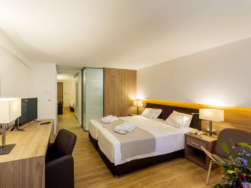 Helles Hotelzimmer mit Doppelbett, zwei Nachttischen, Schreibtisch und Stuhl, moderne Einrichtung.