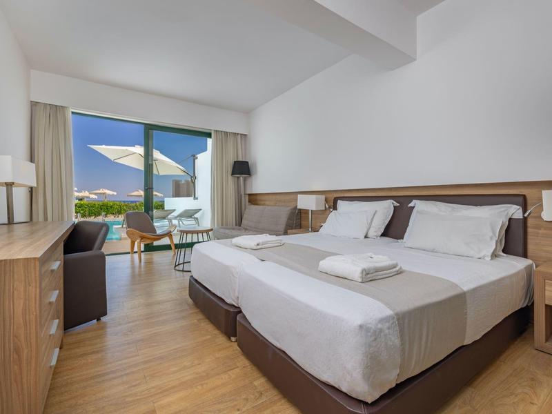 Helles Hotelzimmer mit zwei Einzelbetten, Holzboden und Balkon mit Meerblick.