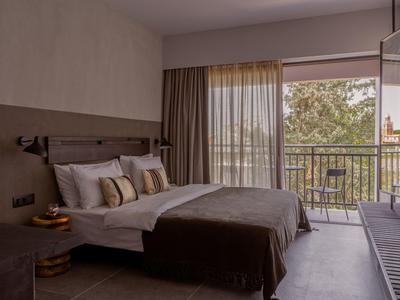 Modernes Schlafzimmer mit großem Doppelbett, Balkon und braunen Vorhängen, natürliches Licht strömt herein.