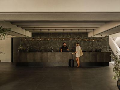 Hotel-Lobby mit Rezeption, dunkelgrauer Theke und zwei Personen, eine mit Reisekoffer.