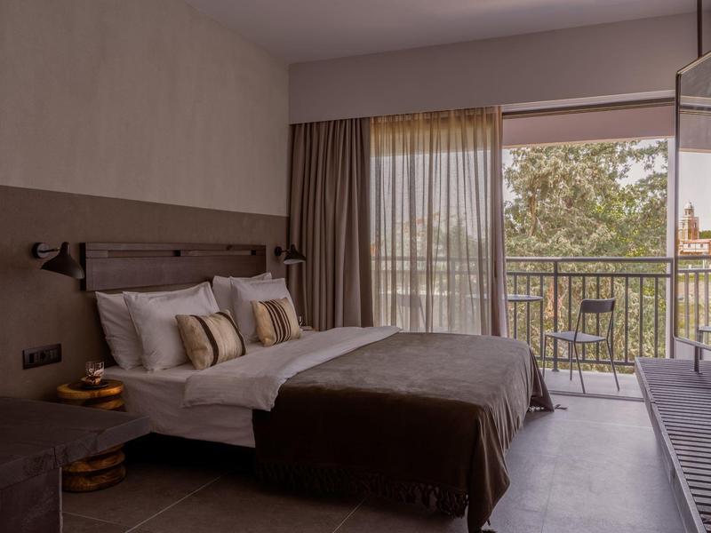 Camera d'hotel moderna con letto matrimoniale e balcone con vista sugli alberi.