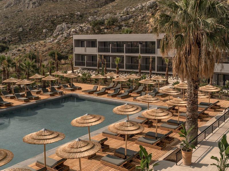 Piscina dell'hotel con lettini e ombrelloni di paglia davanti a una montagna