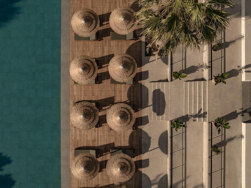 Vista aerea di una piscina dell'hotel con lettini e ombrelloni su una terrazza accanto agli alberi.